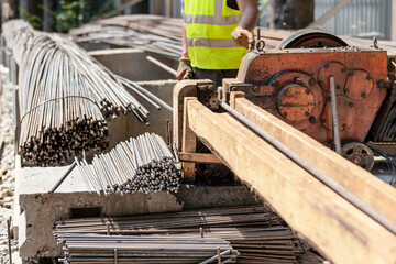 Rebar Rods Cutting on Construction Site. Construction Worker Cutting Metal Reinforcement Rebar Rods with Hydraulic Industrial Cutting Rebar Machine at Building Site. 