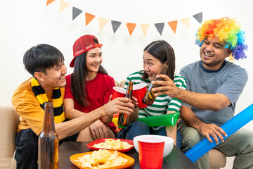 Group of asian friends man and woman watching cheering football match on TV at home. Eating snack and drinking beer. Sport fans people shouting and celebrating sport team victory match.