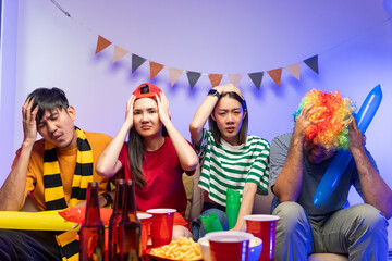 Fototapeta premium Sports fans feel sad when the team they support loses. Group of asian friends man and woman watching cheering football match on TV at home. Eating snack and drinking beer.