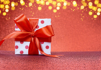 White gift box with polka dots with red bow stands on shiny background. Defocused lights. Christmas, New Year, Saint Valentine, March 8, Mother's Day, birthday. Copy space