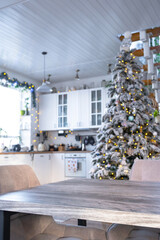 Grey Wooden empty table to demonstrate product with space for text with upholstered chairs in white kitchen, modern interior with Christmas tree and fairy lights. New Year, Christmas mood, cozy home.