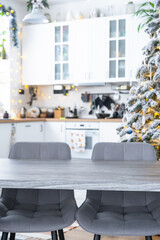 Grey Wooden empty table to demonstrate product with space for text with upholstered chairs in white kitchen, modern interior with Christmas tree and fairy lights. New Year, Christmas mood, cozy home.
