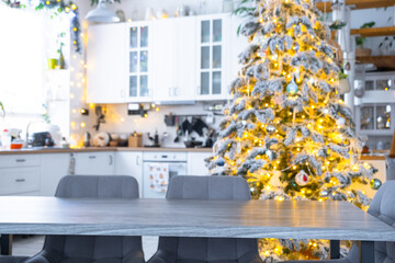 Grey Wooden empty table to demonstrate product with space for text with upholstered chairs in white kitchen, modern interior with Christmas tree and fairy lights. New Year, Christmas mood, cozy home.