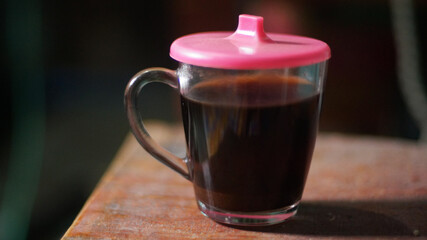 close up of a cup of black coffee in a glass mug with a pink lid, perfect for warming up on a cold winter day