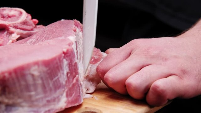 A butcher removes the fascia from a beef steak with a large knife in a dark room