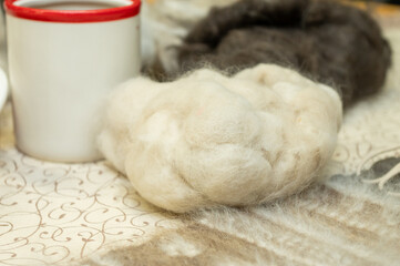 Soft wool fibers and red-rimmed mug on ornate tablecloth