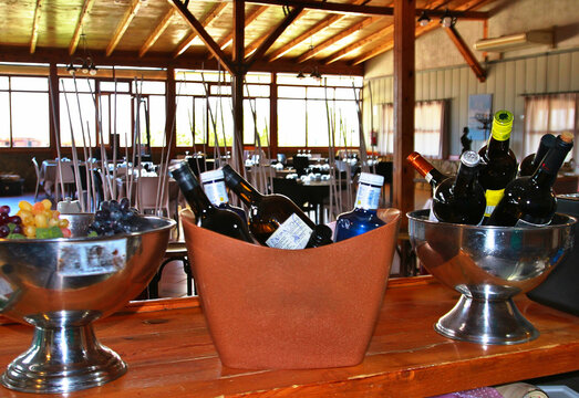 Interior de un restaurante r&uacute;stico en madera con botellas en la barra en primer plano y ventanas al fondo