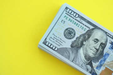 Big amount of hundred dollar bills in thick stack lies on bright yellow color paper background