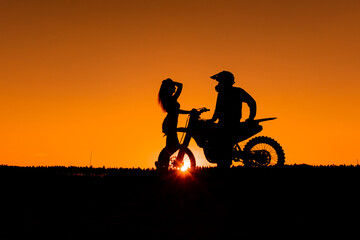 Silhouette of a girl and a man on a motorcycle. Silhouette of a couple and a motorcycle at sunset. Silhouette of a motorcycle racer and a girl at sunset.