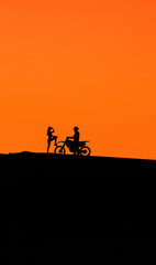 Fototapeta premium Silhouette of a girl and a man on a motorcycle. Silhouette of a couple and a motorcycle at sunset. Silhouette of a motorcycle racer and a girl at sunset.