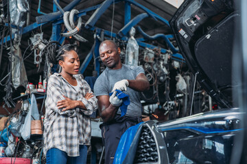 Man Explaining Car Repair to Woman in Busy Automotive Workshop During Daylight Hours