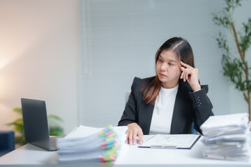 Businesswoman is having headache and touching her head while working with laptop and paperwork in office, she is stressed and tired from work