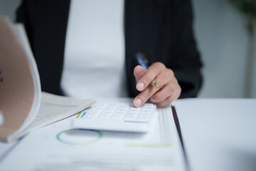 Businesswoman is calculating financial data using calculator and holding pen while working in office, analyzing business growth by looking at charts and graphs