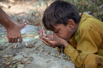 Young Boy Drinking Water From Hands Outdoors, A Helping Hand Pours Water From a Bottle in a Rural Setting