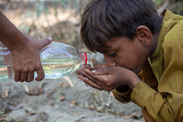 Young Boy Drinking Water From Hands Outdoors, A Helping Hand Pours Water From a Bottle in a Rural Setting