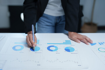 Businesswoman analyzing and pointing at financial statistics displayed on charts and graphs using pen, focusing on investment and financial data analysis for business growth and success
