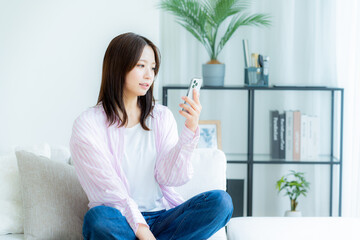 部屋でスマホを操作する若い女性