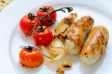 Pork fried sausages with tomatoes on a white plate for a delicious lunch.