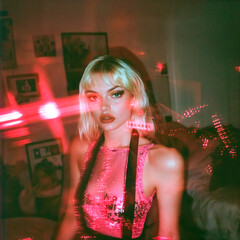 Alternative young blonde woman in home party. Girl posing in apartment at night, lit by red laser lights, with double exposure, moody atmosphere. Grainy texture, 35mm film photo
