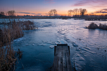 Fototapeta premium A small wooden bridge in front of a frozen lake during sunset, Stankow, Lubelskie, Poland