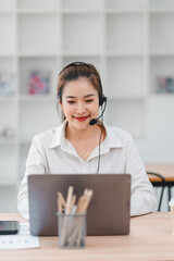 Smiling woman working with headset and laptop at desk