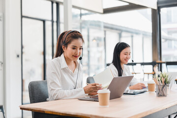 Two women working in modern office with headsets and laptops