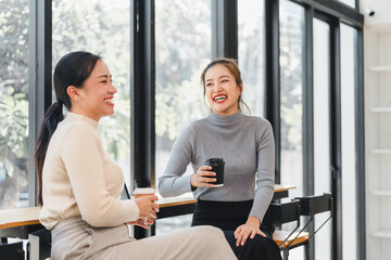 Two women smiling and chatting while holding coffee cups indoors