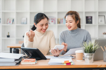 Two women discussing work at desk with documents and devices