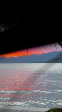 Vertical video of beautiful Lake Garda, Italy in the evening at magical colorful sunset, palm trees in the background add mystical view, Dolomites mountains, Alps are visible, romantic sky atmosphere