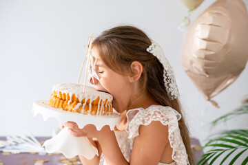 little girl in a beautiful white dress bites a cake