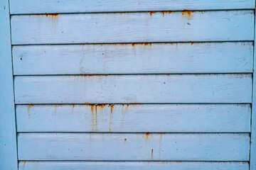 Fototapeta premium A weathered blue wooden wall with horizontal planks, showing rust stains and aged texture. The surface displays natural imperfections, scratches, and streaks, reflecting decay and vintage aesthetics. 