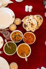 Indisches Essen auf einem Tisch mit roter Tischdecke in vier Schälchen verschiedene Sorten, da Gemüse dazu nahen Brot, teller, Wasser und Salz und Pfeffer,gewürz auf dem Tisch