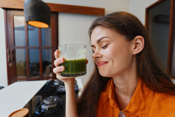 Young woman enjoying green healthy juice in a cozy kitchen, promoting healthy lifestyle and wellness concepts, with a cheerful expression and vibrant colors