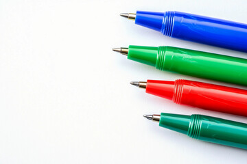 Quatre stylos à bille aux couleurs vives (bleu, vert, rouge et turquoise) sont alignés horizontalement, pointes tournées vers la gauche, sur un fond blanc épuré.