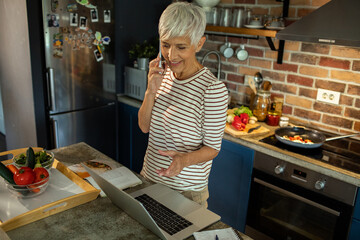 Senior woman cooking in kitchen while talking on phone