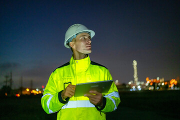 Worker in Bright Safety Gear Utilizing a Tablet While Inspecting a Construction Site at Night,...
