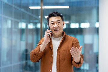 Asian man mature businessman engaging on a smartphone call, appearing cheerful and animated while interacting, symbolizing communication and professional engagement in a modern work environment.