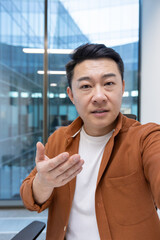 Asian mature businessman engaging in a video call, looking at the camera talking. Located indoors...
