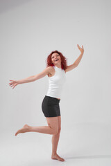 Fototapeta premium A woman with red hair poses for the camera with a smile on her face, she is wearing a white T-shirt and a black skirt. She has a beautiful figure. Fitness and healthy eating concept.