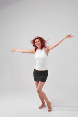 A woman with red hair poses for the camera with a smile on her face, she is wearing a white T-shirt and a black skirt. She has a beautiful figure. Fitness and healthy eating concept.