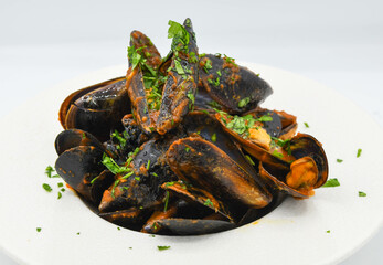 Mejillones cocidas en sartén con perejil sobre fondo blanco.