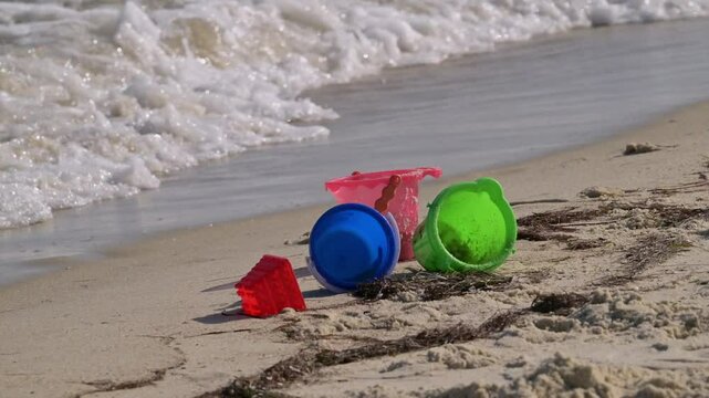 colorful toy plastic buckets in sand on beach with waves in background
