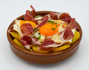 Huevos fritos con patatas y jamón curado sobre fondo blanco