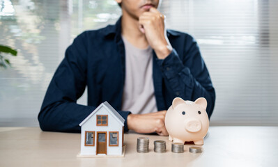 thoughtful person considers financial planning with piggy bank and house model