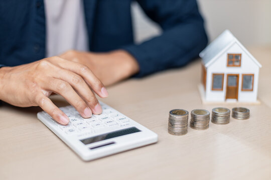 Person calculating finances with coins and house model on table