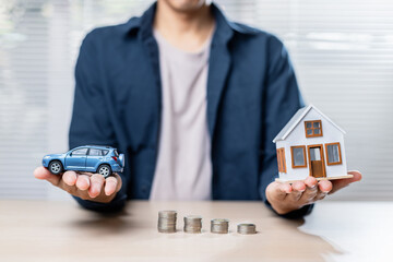 person holding car model and house model with coins on table