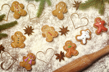 Embellished with icing, a cheerful assortment of gingerbread cookies is set on a floured surface, surrounded by pine branches, star anise, and heart shapes, evoking a warm holiday spirit. 