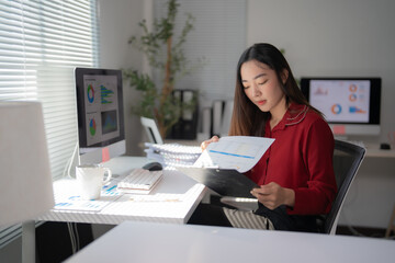 Focused asian businesswoman reviewing financial reports and data analysis on clipboard and...
