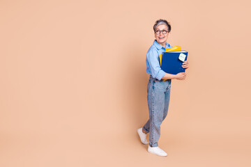 Elderly woman in casual fashion holding folders on a beige background, conveying happiness and...