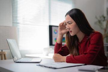 Young office worker experiencing a headache while tackling a challenging project on her laptop,...